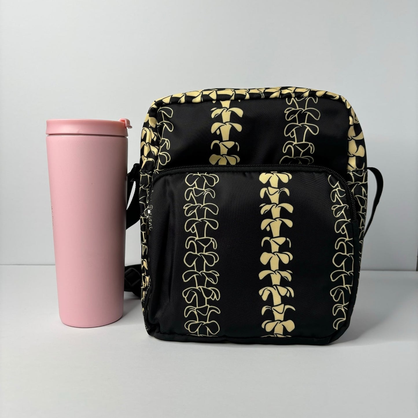 Crossbody bag by Puakenikeni Designs, in black with the best-selling pua kenikeni lei design, Kaulua; for women, moms, teenage girls, for travel and school Beige Lei Design next to 24 oz tumbler