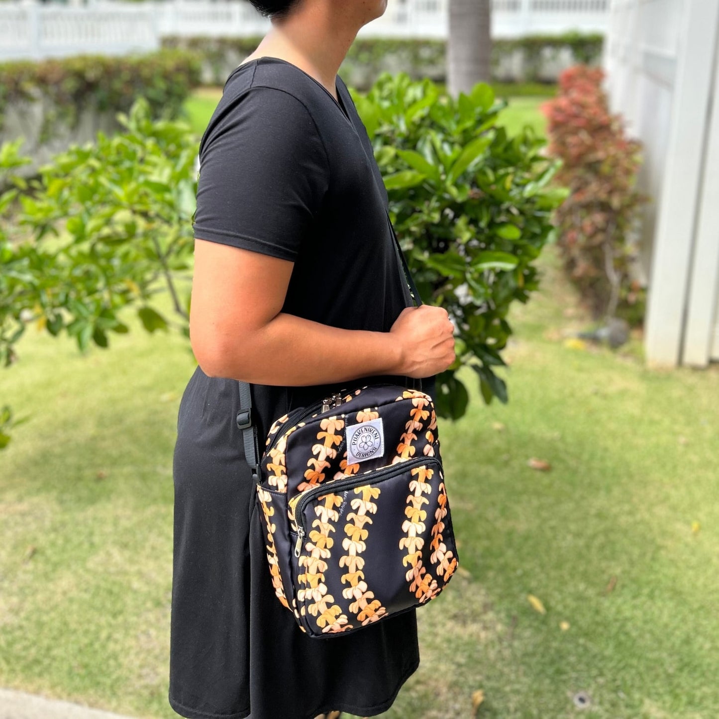 Crossbody bag by Puakenikeni Designs, in black with the best-selling pua kenikeni lei design, Kaulua; for women, moms, teenage girls, for travel and school, on model