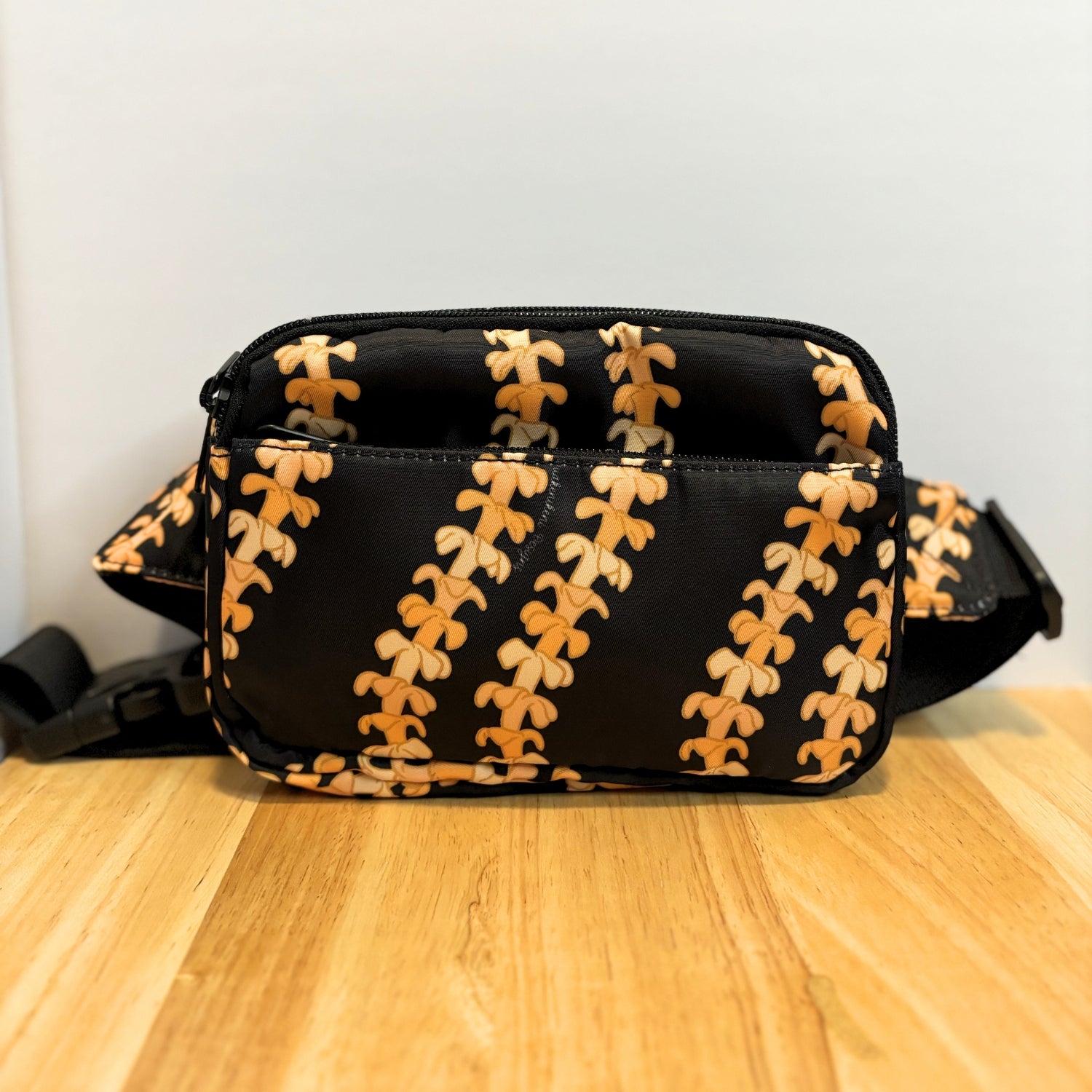 fanny pack, waist bag, belt bag, chest bag, hip pack, crossbody in orange pua kenikeni lei on black from Puakenikeni Designs on table
