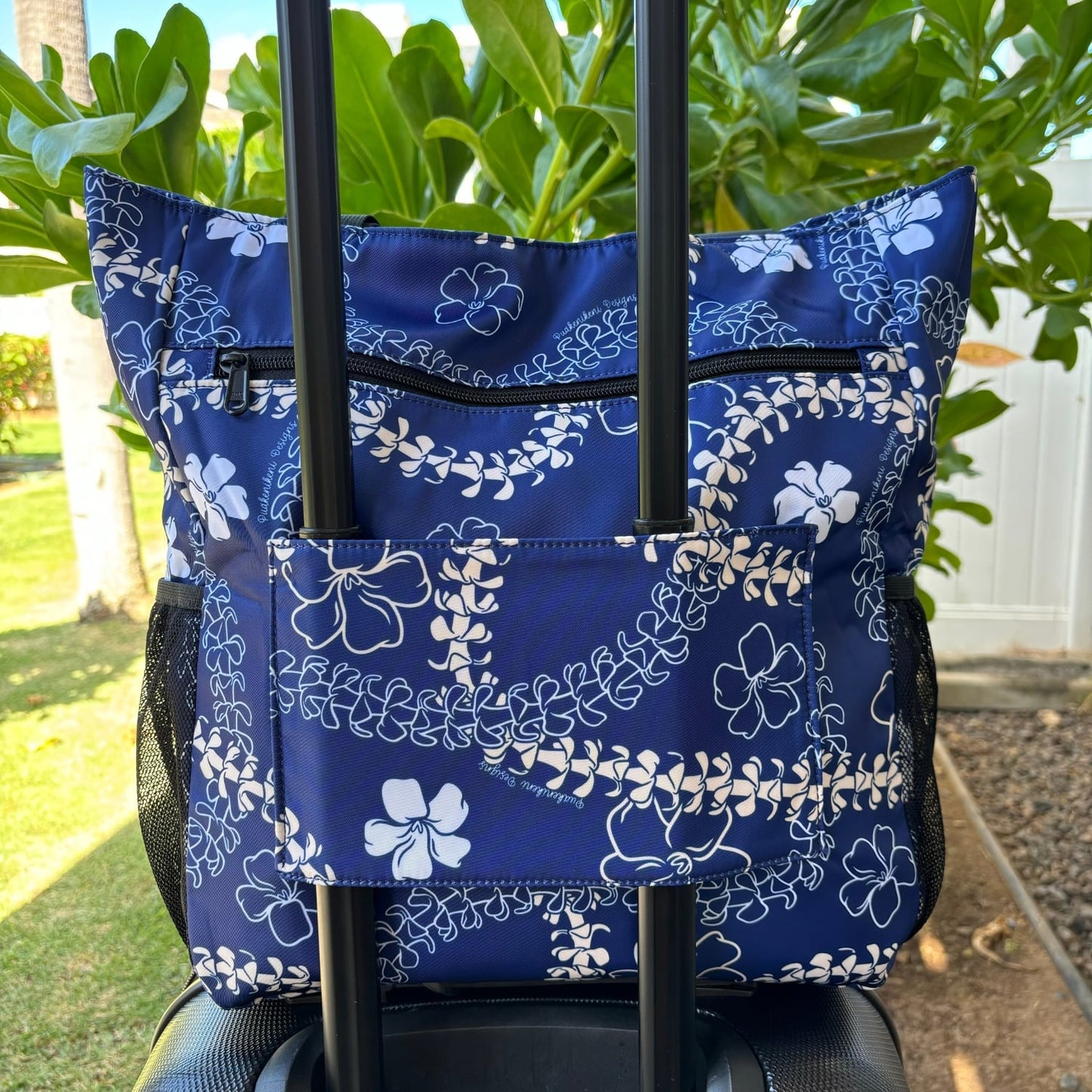 holoholo bag with pua kenikeni lei and flowers in blue from Puakenikeni Designs back view on sliding luggage suit case carry-on