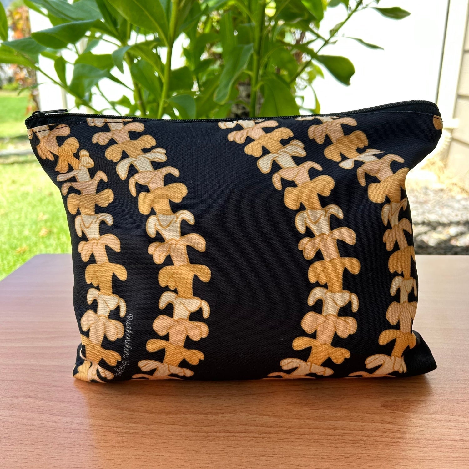 Puakenikeni lei canvas zipper pouch - black with orange lei - on a table