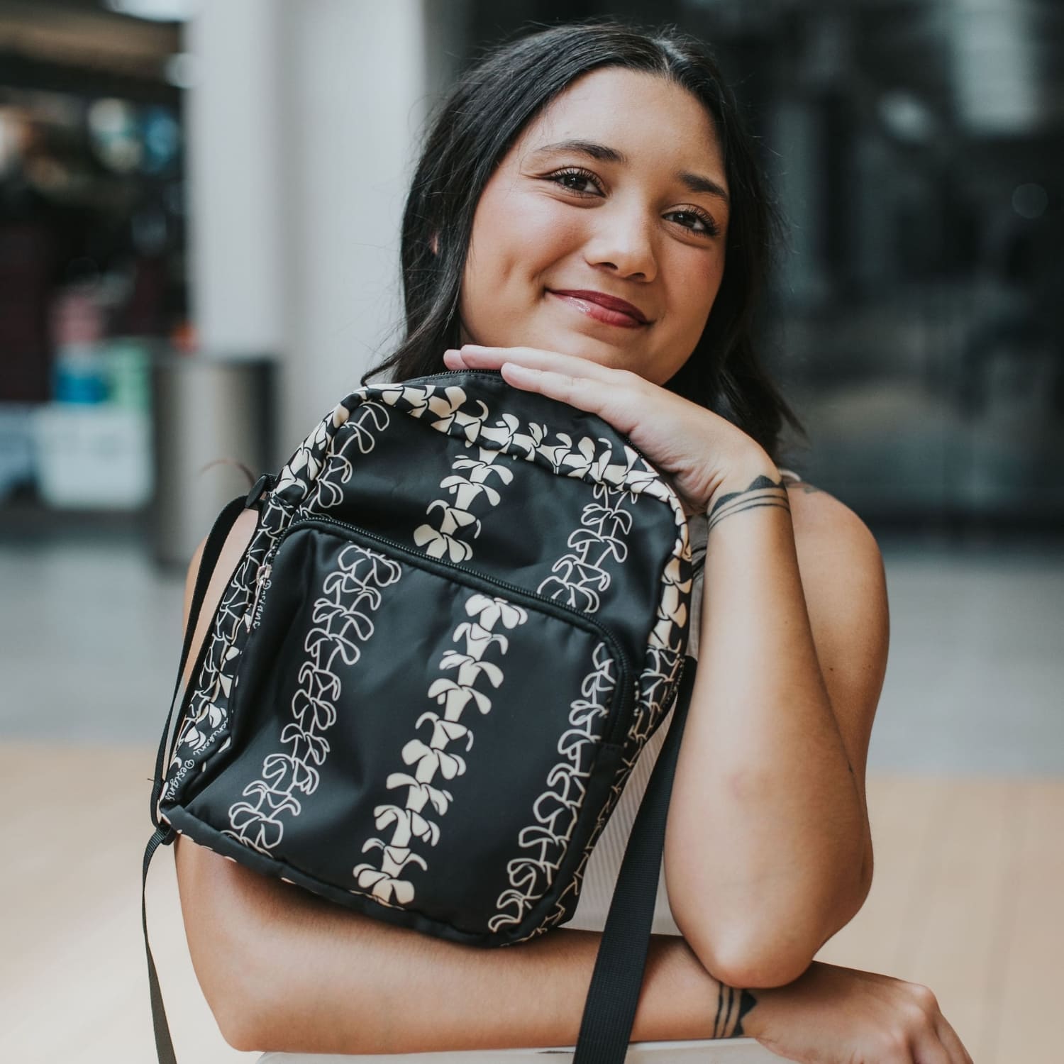 Crossbody bag by Puakenikeni Designs, in black with the best-selling pua kenikeni lei design, Kaulua; for women, moms, teenage girls, for travel and school Beige Lei Design model holding close up