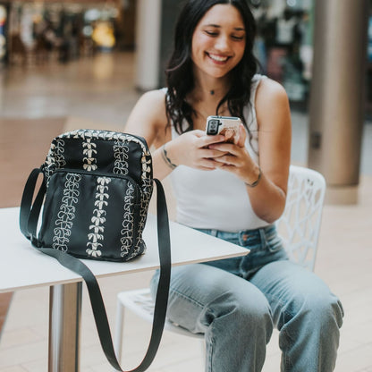 Crossbody bag by Puakenikeni Designs, in black with the best-selling pua kenikeni lei design, Kaulua; for women, moms, teenage girls, for travel and school Beige Lei Design on table