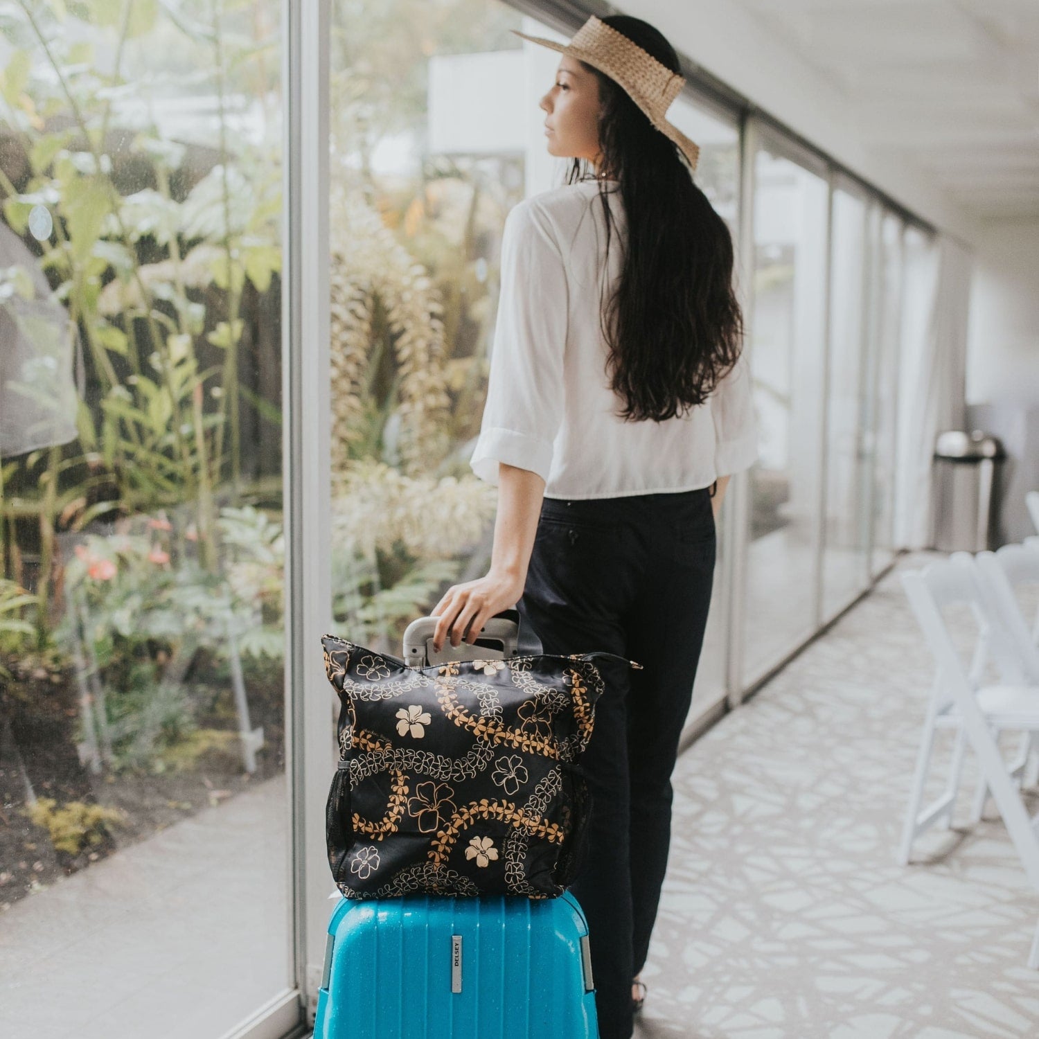 Holoholo bag with orange pua kenikeni lei from Puakenikeni Designs on luggage, model walking down the lobby traveling