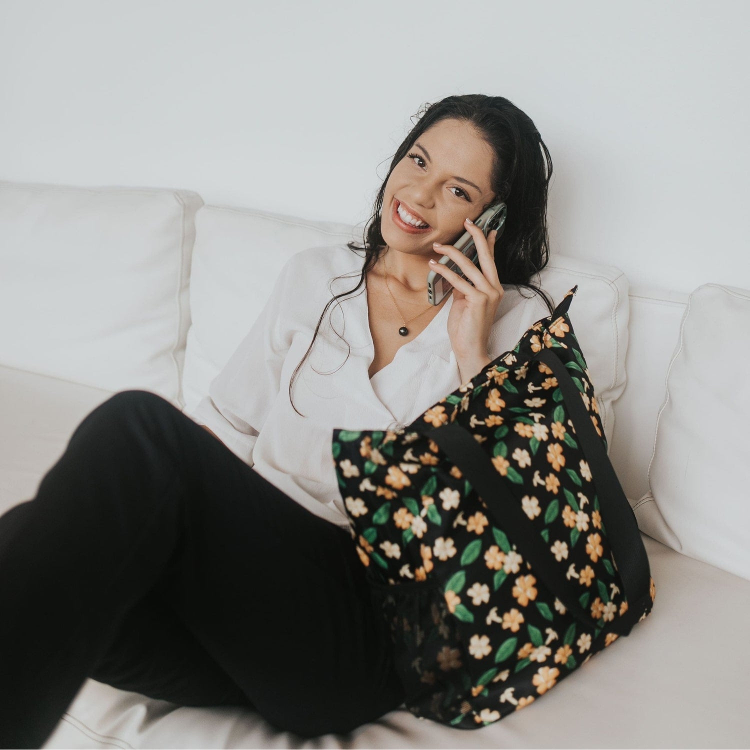 Holoholo bag with pua kenikeni flowers and leaves from Puakenikeni Designs model on couch on the phone