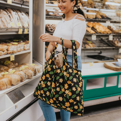 large foldable reusable shopping bag with puakenikeni flowers and leaves from Puakenikeni Designs - model using grocery shopping